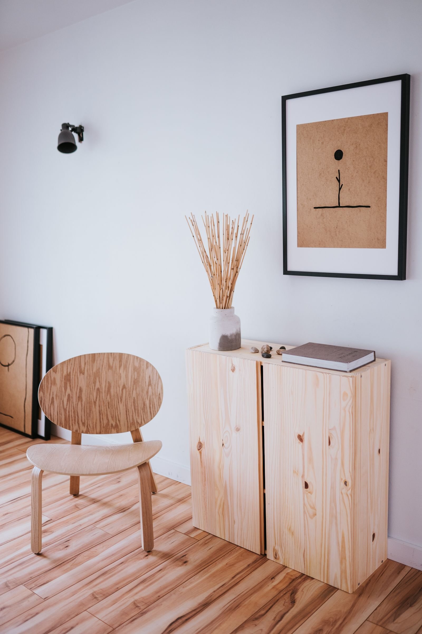 Canto de descanso minimalista em madeira clara, com cadeira, vaso com hastes secas e quadro simples