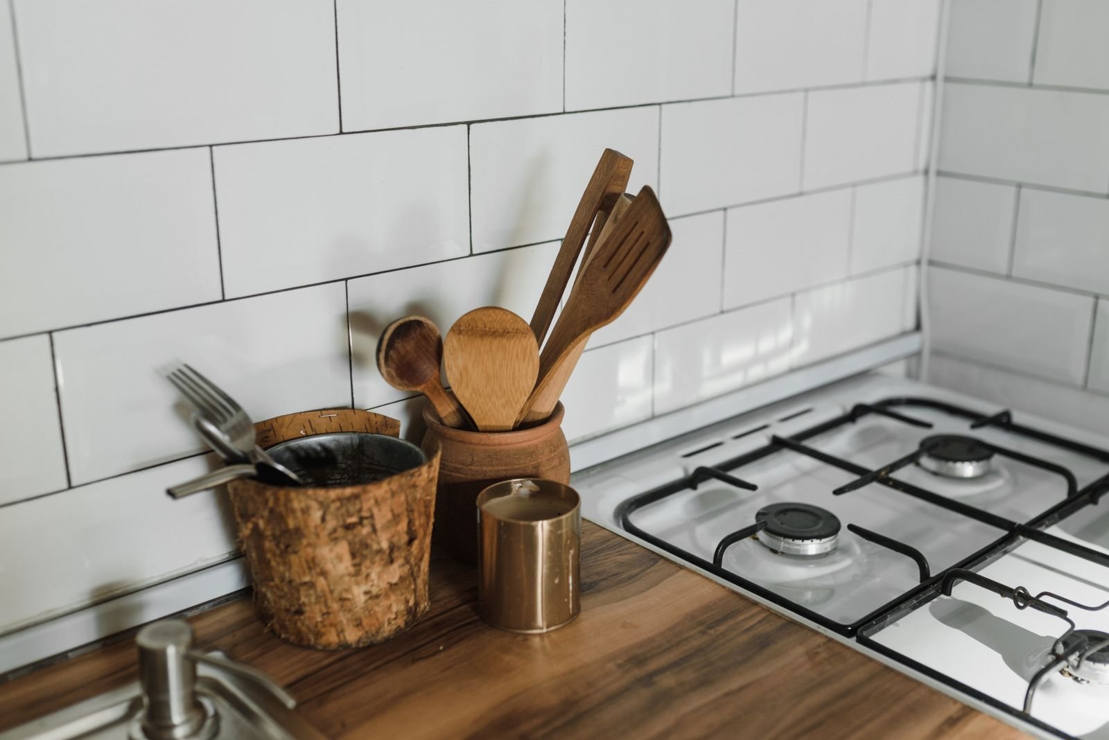 Canto de cozinha com azulejo branco, bancada de madeira, utensílios de pau em potes de cerâmica e fogão a gás limpo