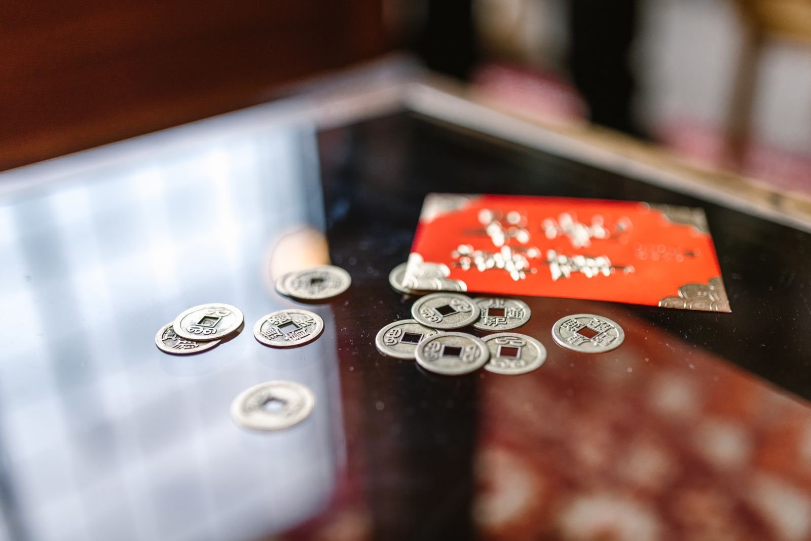 Moedas chinesas antigas de furo quadrado espalhadas sobre mesa escura, ao lado de envelope vermelho
