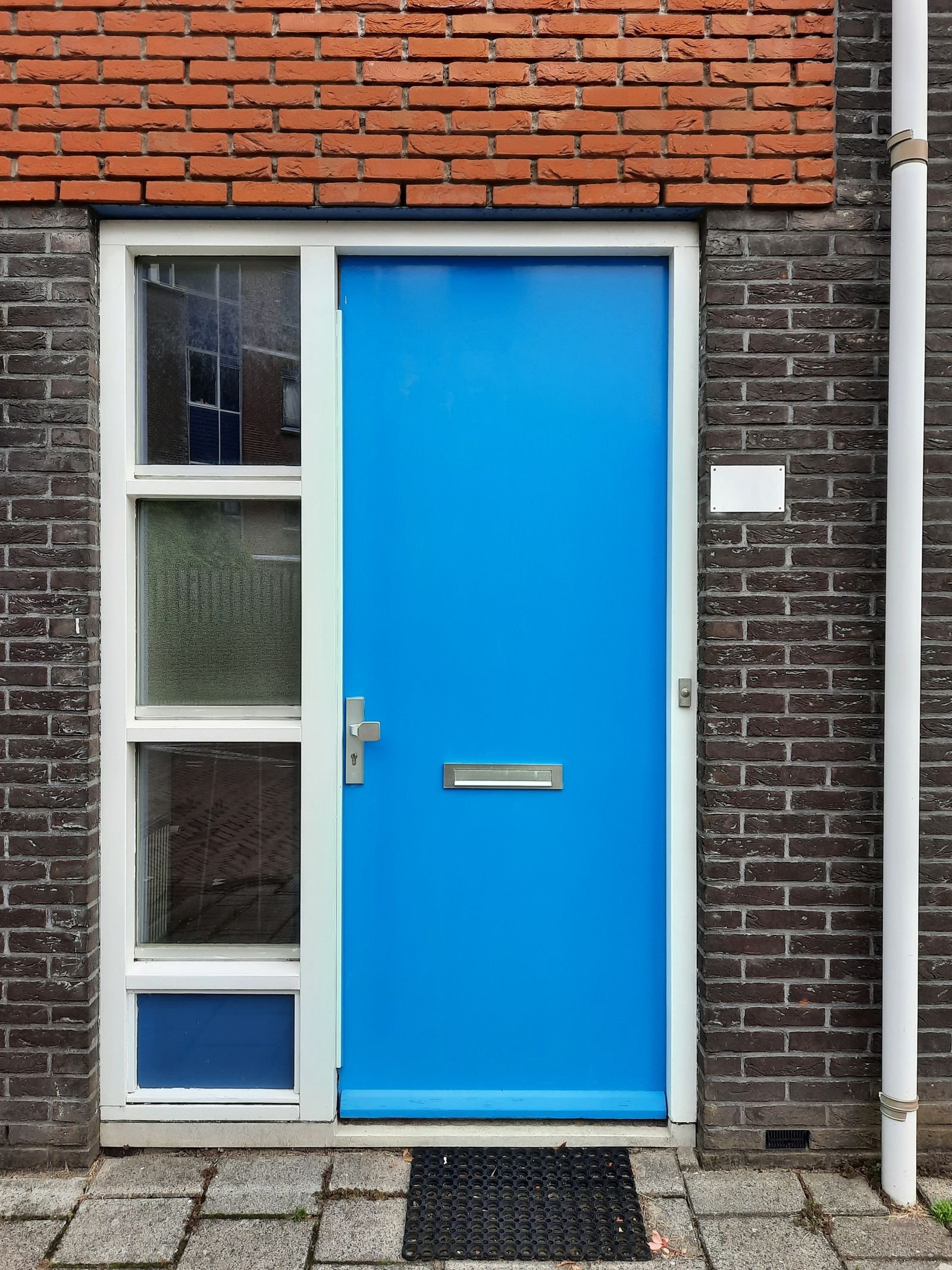 Porta de entrada azul vibrante em fachada de tijolo aparente, com fechadura moderna