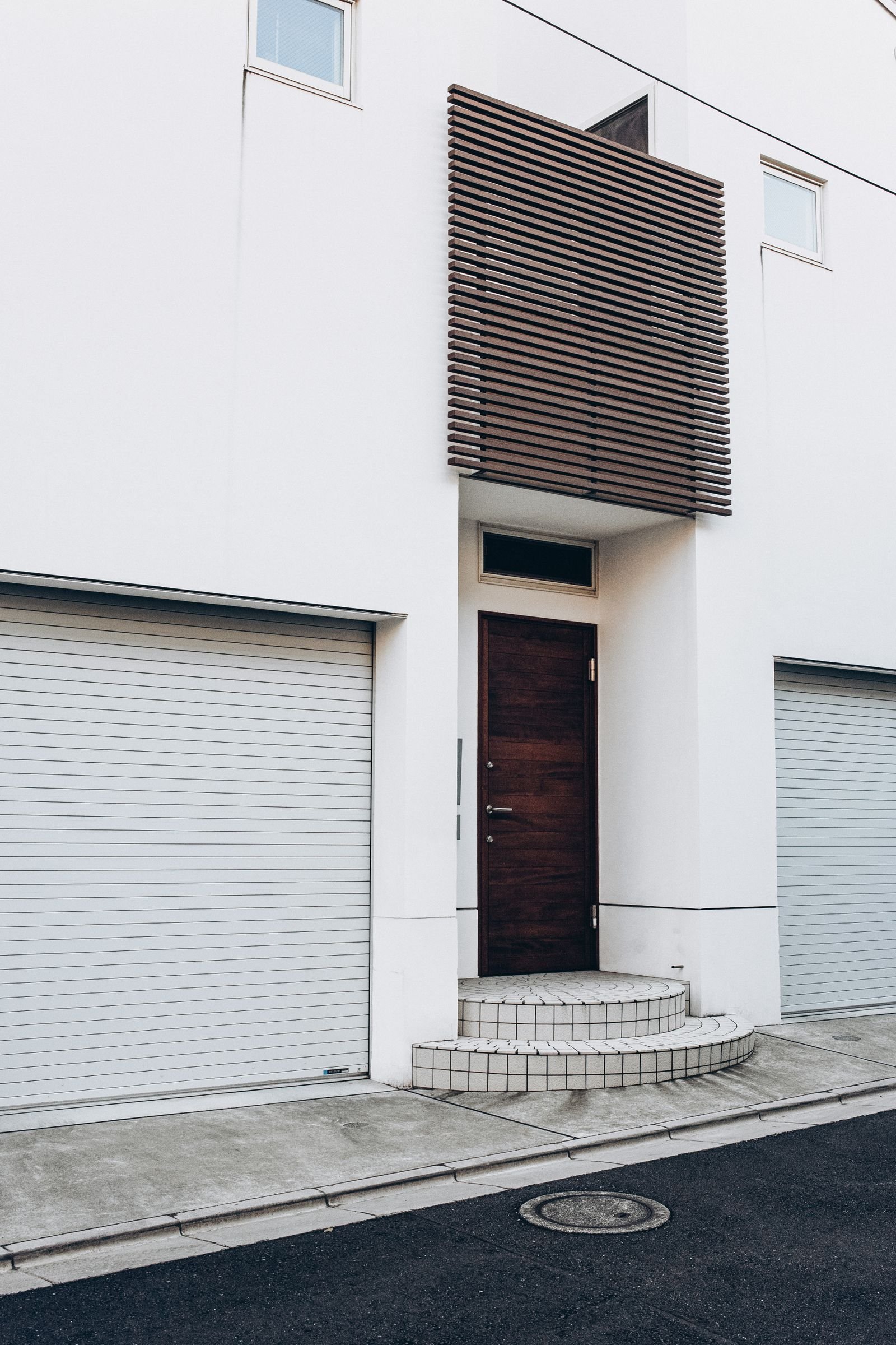 Porta de madeira escura em fachada branca minimalista, com brise vazado de madeira e escada de acesso