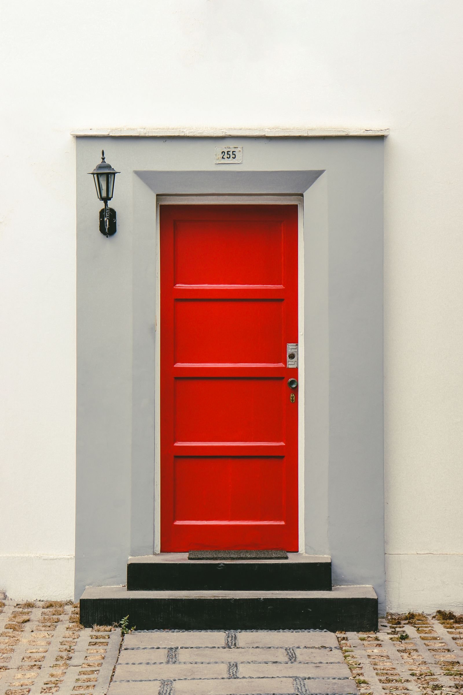 Porta vermelha vibrante em fachada branca minimalista, com luminária lateral