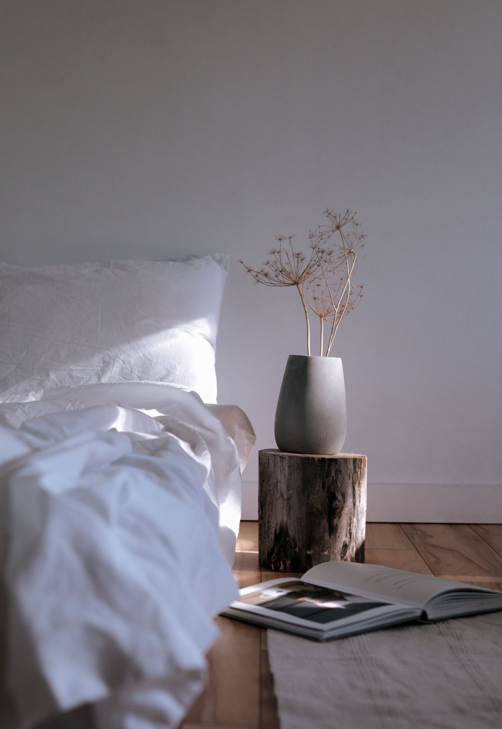 Quarto sereno e minimalista, com roupa de cama branca, madeira natural e luz suave da manhã