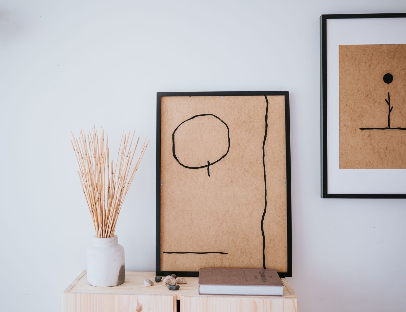 Detalhe de decoração de sala com vaso claro, arte minimalista e madeira clara em tons neutros