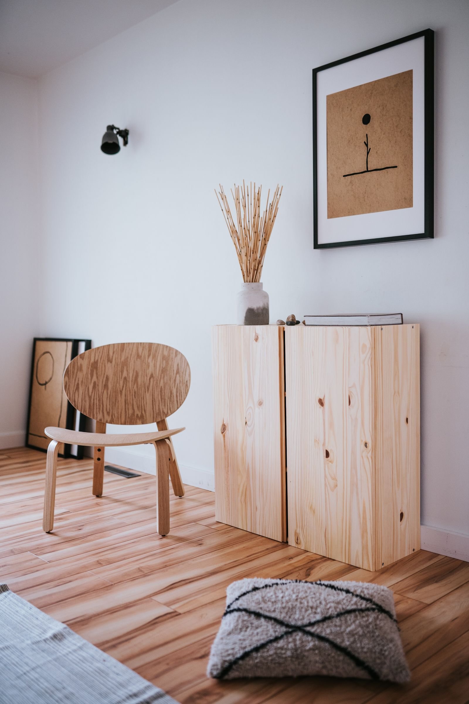 Sala de estar clara em estilo japandi, com madeira clara, poltrona, arte minimalista e muita luz