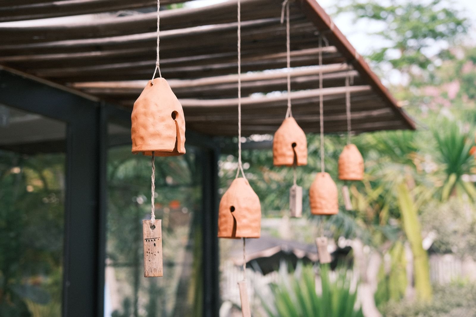 Sinos de cerâmica terracota pendurados numa pérgula moderna de vidro e aço, com jardim ao fundo